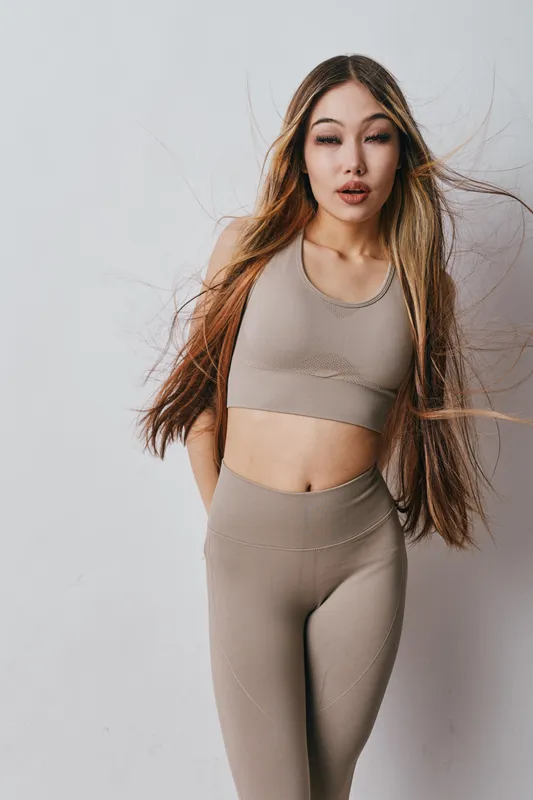 Young woman in beige sportswear posing with long flowing hair on light background. Fitness, fashion and confident model in activewear for healthy lifestyle and wellness.