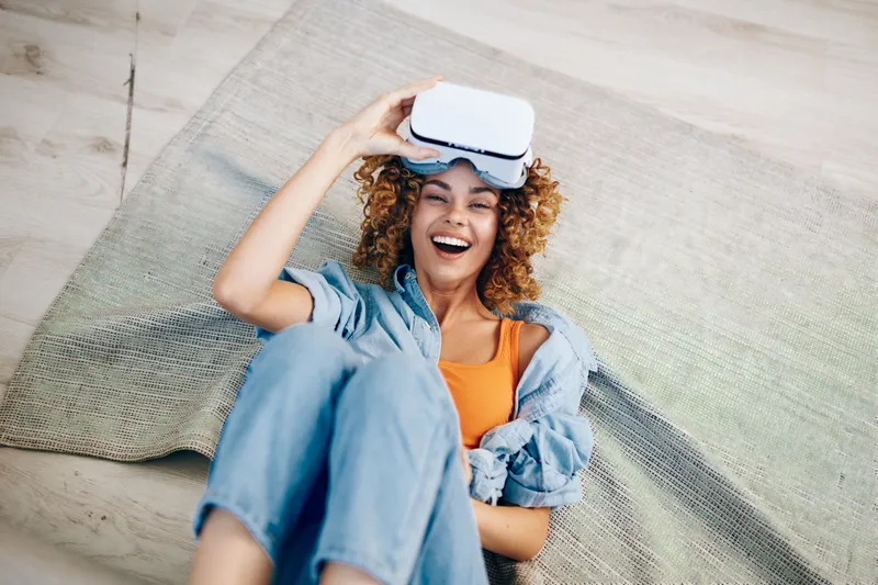 Улыбающаяся женщина наслаждается игрой в виртуальной реальности в VR-очках дома, в помещении