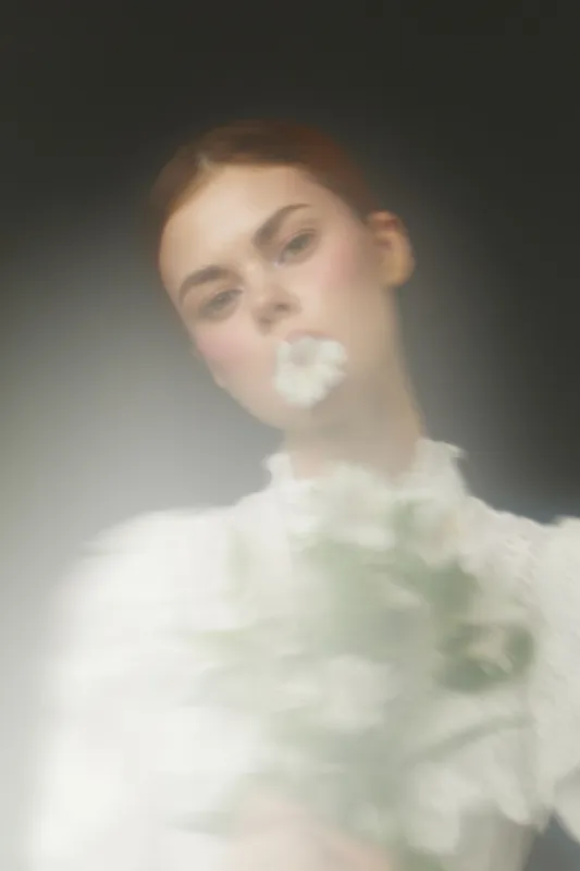 Ethereal portrait of a young woman holding white flowers, capturing delicate emotions and soft light amidst a dreamy, blurred background