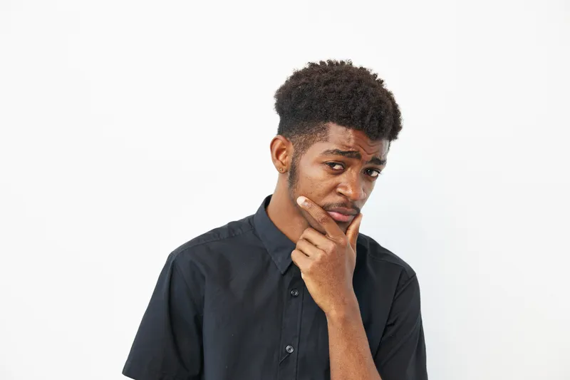 Thoughtful African American man posing confidently with a hand on his chin, wearing a casual black shirt. The clean background enhances his expression and style.