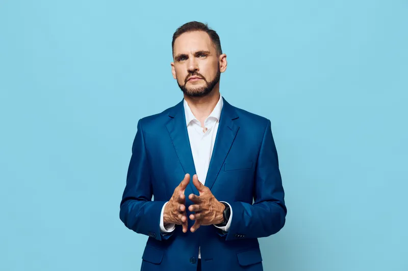 A professional man, poised and confident, stands before a vibrant backdrop, conveying focus, readiness, and calm leadership in a modern business setting.