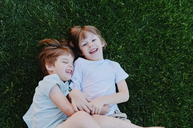 Happy children enjoying a sunny day, smiling while lying on the green grass, creating joyful memories together in a playful atmosphere.