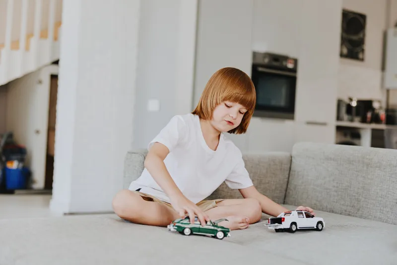 Playful boy enjoying his time indoors while playing with toy cars on a cozy sofa in a modern living space. A scene filled with fun and creativity.