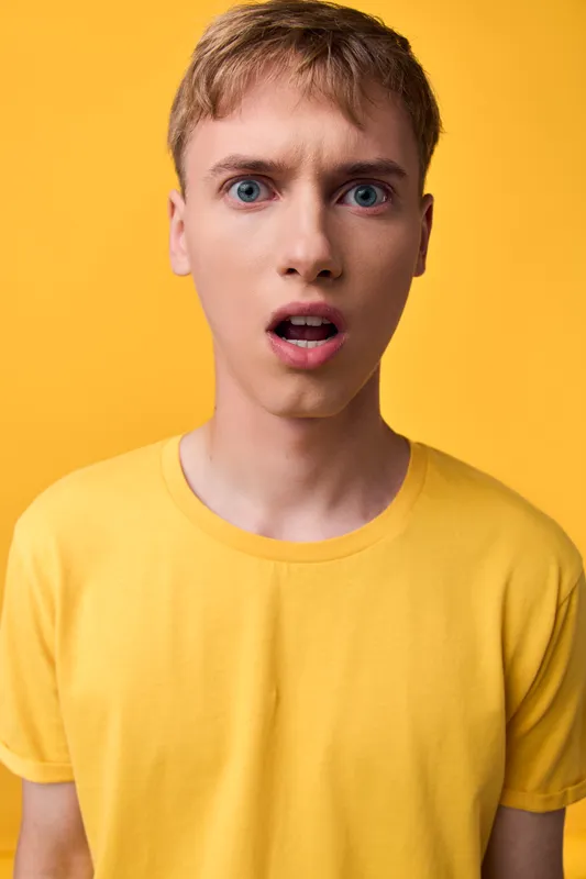 Surprised man in a yellow shirt against a matching yellow background, capturing a bold mood, unexpected moment, and youthful energy for fashion, lifestyle, or expressive stock content