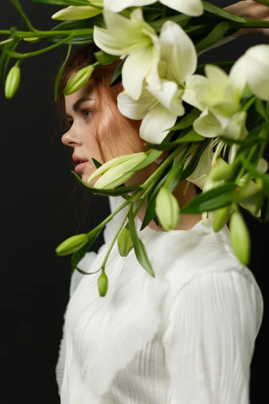 Beautiful young woman with floral headpiece, evoking elegance and nature, wearing a white top, against a dark background, ideal for concepts of beauty and wellness