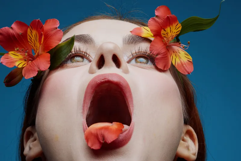Enthusiastic woman with flowers, expressing joy against a vibrant blue background, showcasing a bold seasonal vibe and captivating emotions