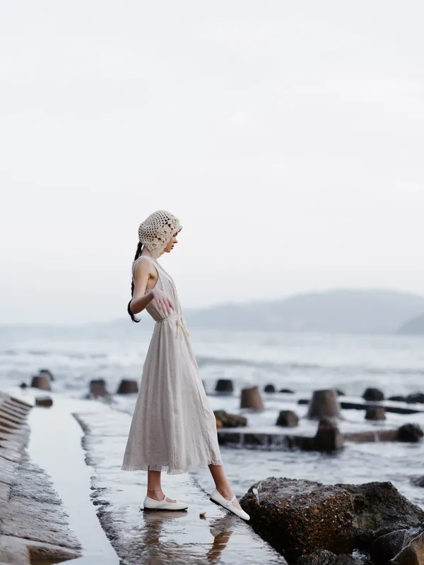 Летняя красота: молодая привлекательная женщина европейской внешности позирует на пляже в модном платье, наслаждаясь свободой и романтической атмосферой заката над океаном