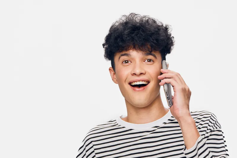 young man talking on phone with happy expression wearing striped shirt against white background, casual communication and positive mood