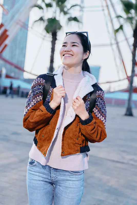 Woman wear jacket in urban street outdoors smiling under sunlight with backpack and denim capturing casual fashion bright day confident mood and lively vibe