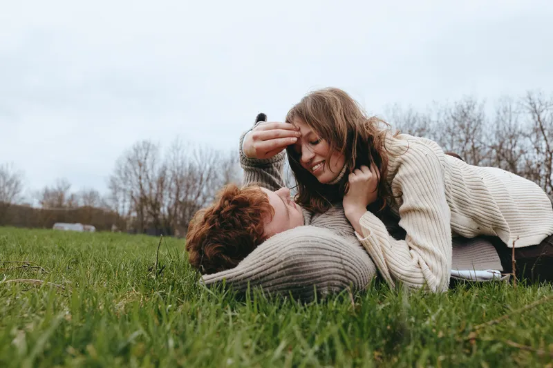 Couple affection outdoors grass sweaters lifestyle romance connection candid moment expressing relaxation happiness in a sunny field