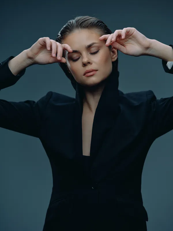 Calm woman with closed eyes wearing black clothing in a studio setting expressing relaxation and serenity.
