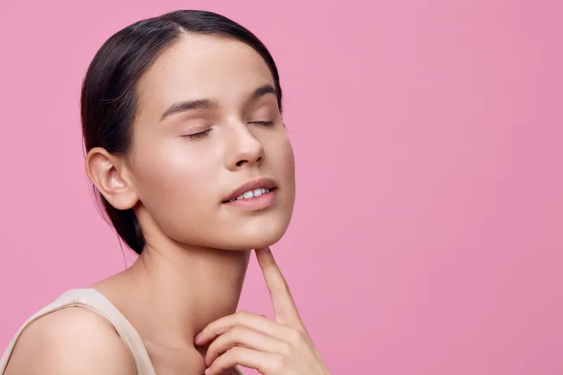 Young woman with closed eyes enjoying beauty on a pink background, showcasing serene emotions and minimalist fashion for wellness and self care