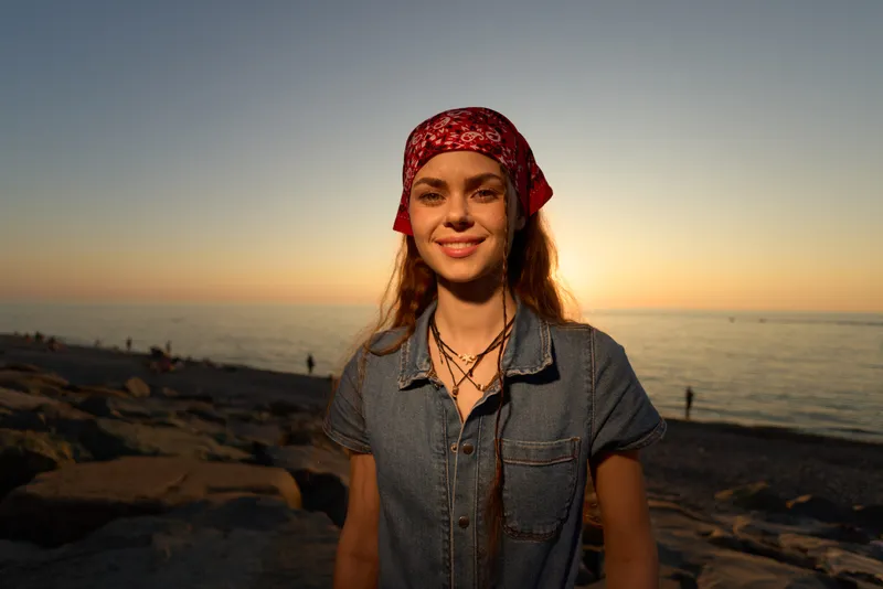 lifestyle woman in modern boho-western denim street style smiling at sunset with warm film color tones and relaxed beach background