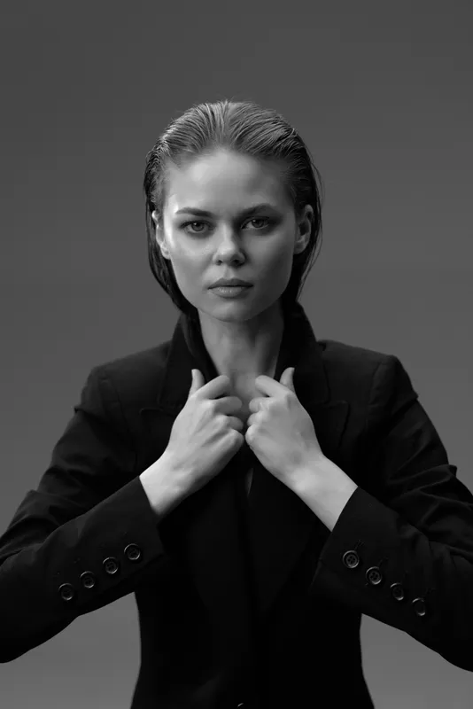 Black and white portrait of serious woman in formal jacket with clasped hands against gray background