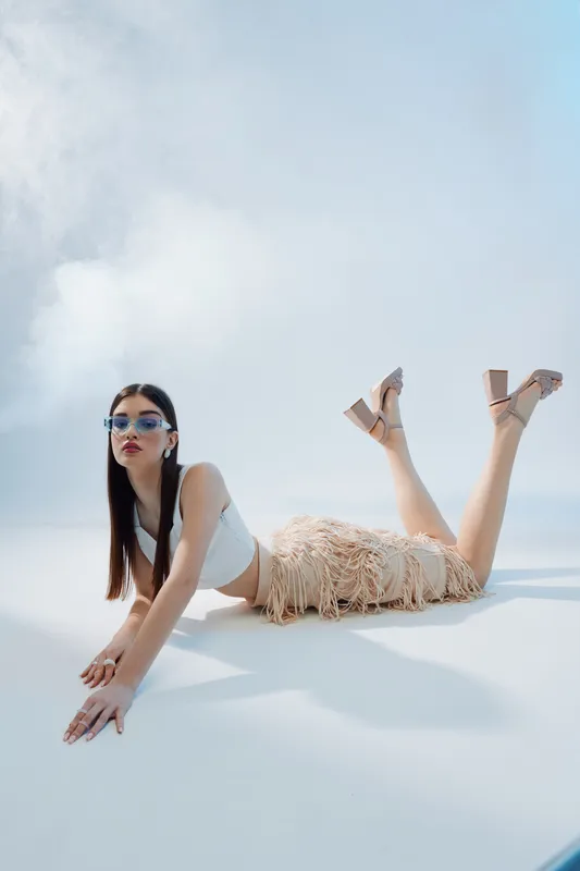 Young woman in fashionable outfit and sunglasses lies on the floor in bright studio. Concept of woman beauty fashion with modern style and confident pose.