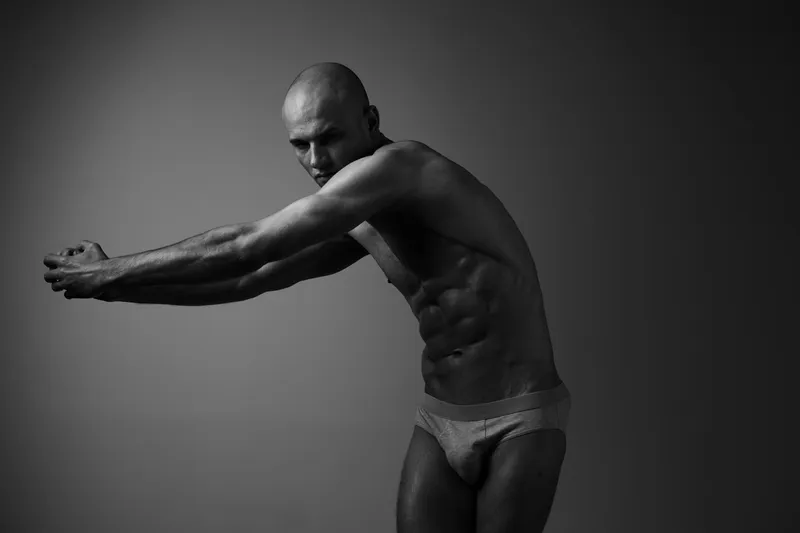 Athletic man posing in a black and white setting, showcasing strength and determination through a powerful stance and expressive body language.