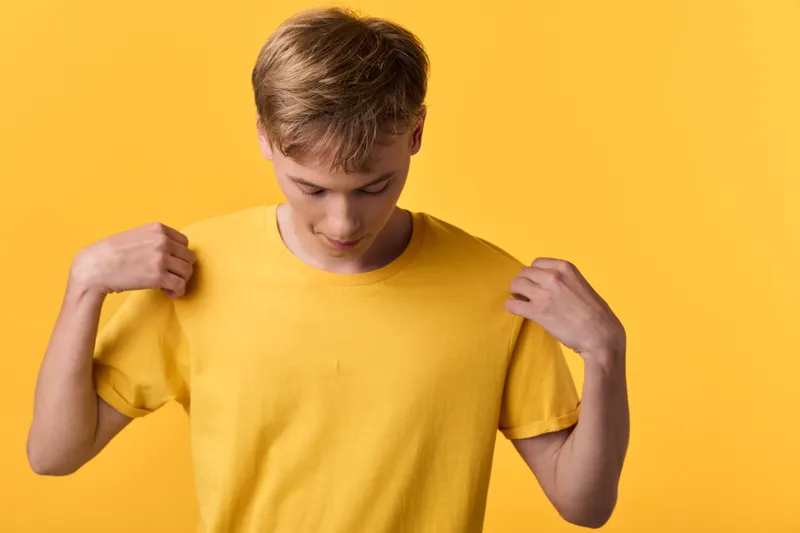 Young man wearing a yellow shirt pulls at the sleeves in a bold studio shot, bright monochrome background, casual fashion, confident mood, clean composition for lifestyle use