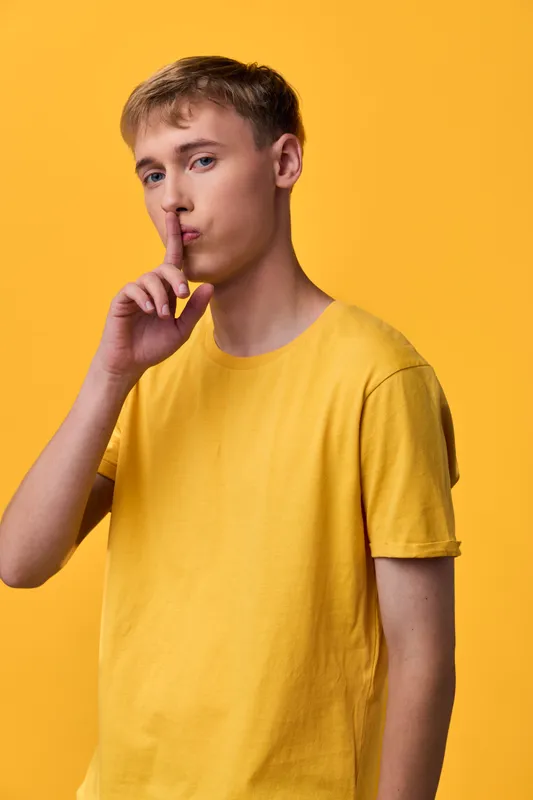 Silence gesture with finger to lips in a bright yellow shirt, studio setting conveying hush, calm and mystery, suitable for lifestyle, fashion, or communication themes, clean background and shallow