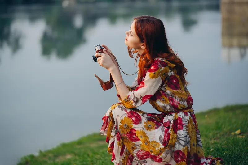 Рыжеволосая женщина с фотоаппаратом на природе у озера
