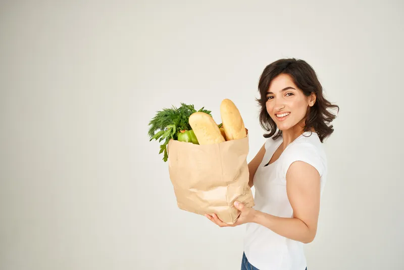 Весёлая брюнетка с бумажным пакетом продуктов и овощей