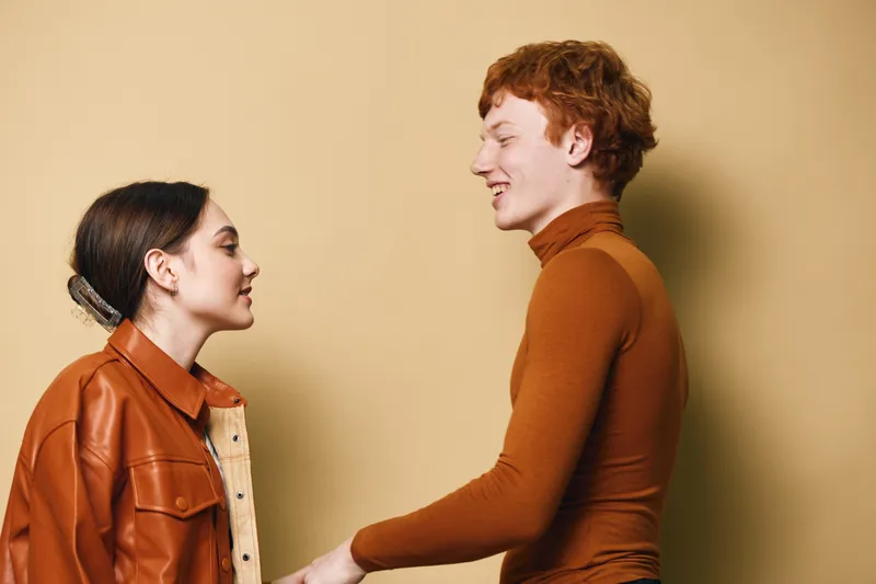 Young man and woman smiling and interacting with each other in casual clothing against beige background with warm lighting for friendship or connection.