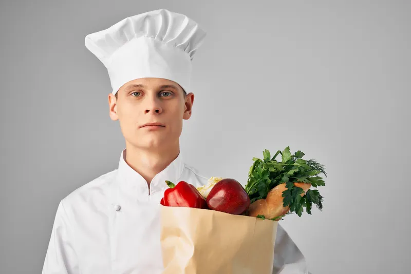 Мужчина с пакетом продуктов для здорового питания работает на кухне ресторана