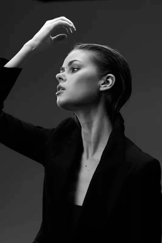 Black and white portrait of a woman with elegant pose and serious expression in formal black attire.