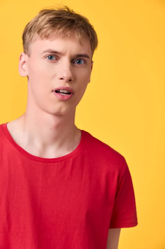 Man with surprised expression wearing a red t shirt against a bright yellow background, highlighting bold colors, casual style, and spontaneous emotion for lifestyle stock