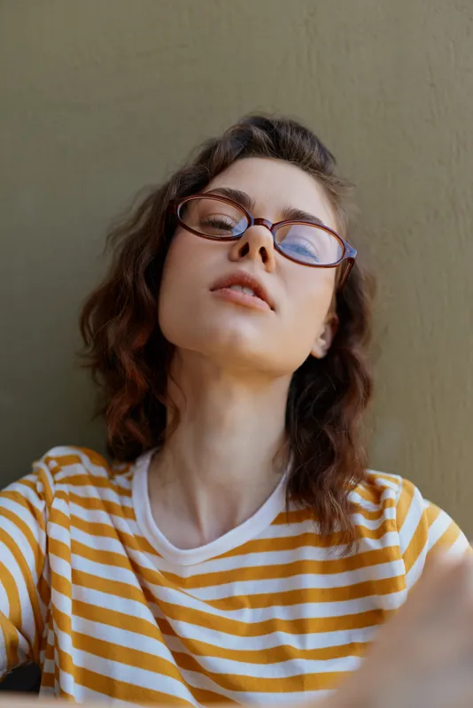 Smiling woman with striped yellow shirt relaxing at home, casual lifestyle indoors, natural light, glasses, warm mood, confident pose, everyday moment, portrait