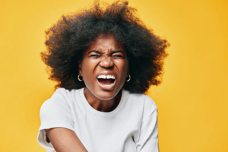 Happy young woman with curly hair showing emotions in front of a bright yellow background, wearing a casual white t shirt Key concepts include joy and self expression