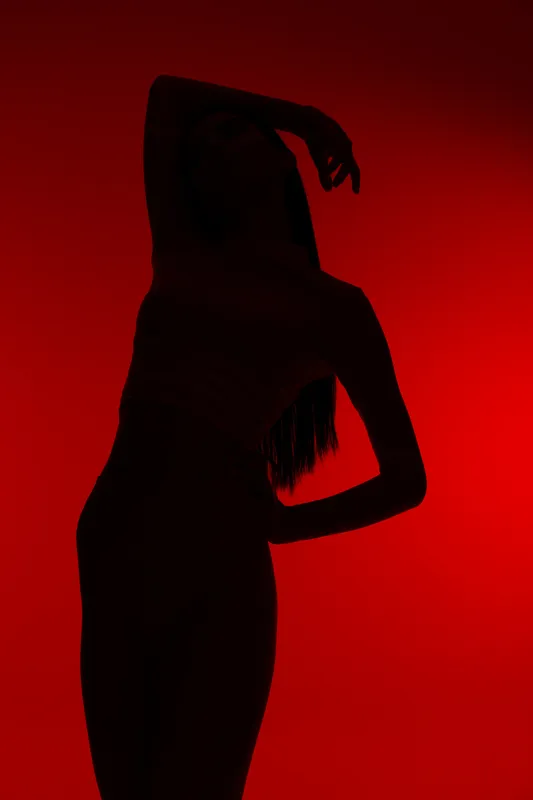 Silhouette of a woman sport fitness pose against vibrant red background, highlighting strength, flexibility, and active lifestyle in dynamic lighting.