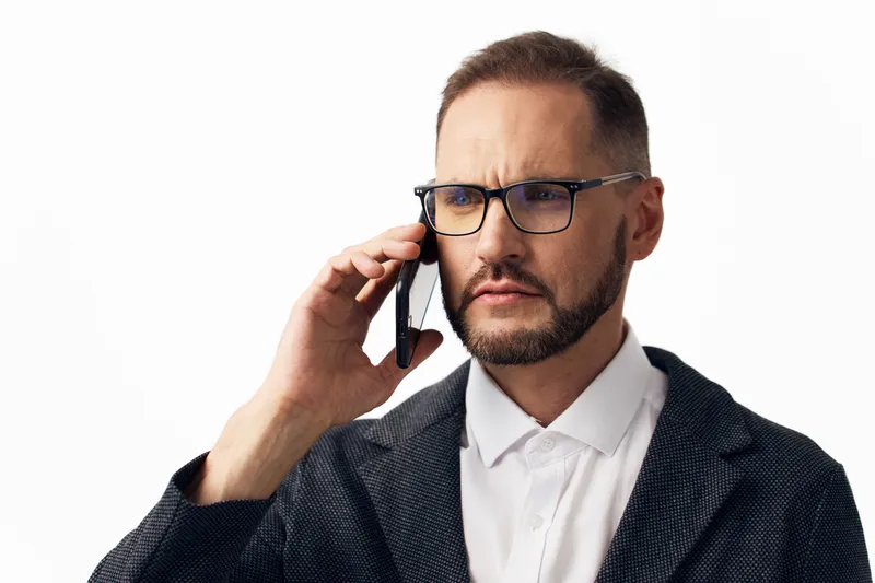 A professional business man speaks on a call, displaying a thoughtful and focused expression, isolated colored background, conveying confidence and serious intent.