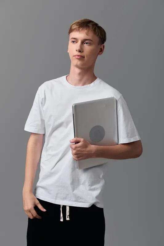 Young man holding a laptop in a white tee, casual style, studio setting, ready for study, learning and digital work across education and tech themes