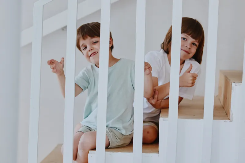 Smiling children sitting on stairs, showcasing playful expressions and joyful interactions. Bright and modern interior creates a cheerful atmosphere for family moments.