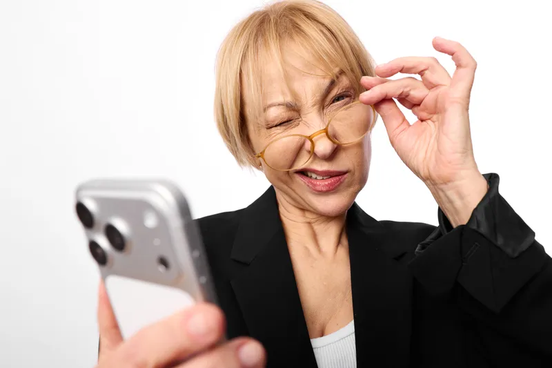 Elderly woman, phone, glasses, crying, stress, business, age, emotion, wiping her eye, frustrated expression, studio portrait on white background, mental distress