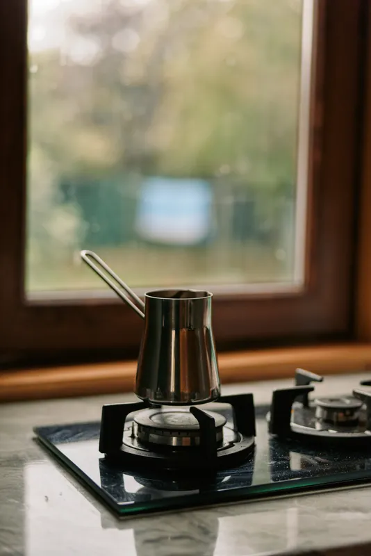Closeup of a metal pot resting on a gas burner in a modern kitchen, showcasing reflective surfaces and a calm, domestic cooking moment, with soft light, warm tones and quiet preparation.
