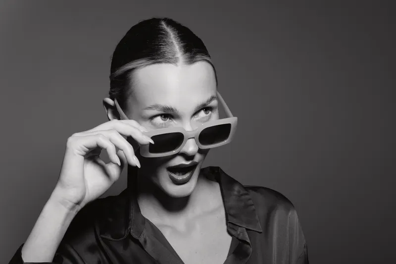 Portrait of young white woman with light skin and slicked hair looking surprised while holding sunglasses in studio. Concept of fashion, beauty, and expression.