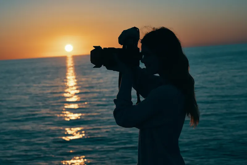 Женщина-фотограф с камерой на закате у моря, природный пейзаж
