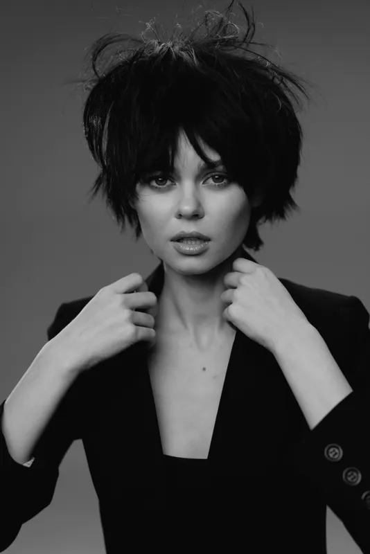 Black and white portrait of a stylish woman with messy short hair wearing a blazer with a serious expression.