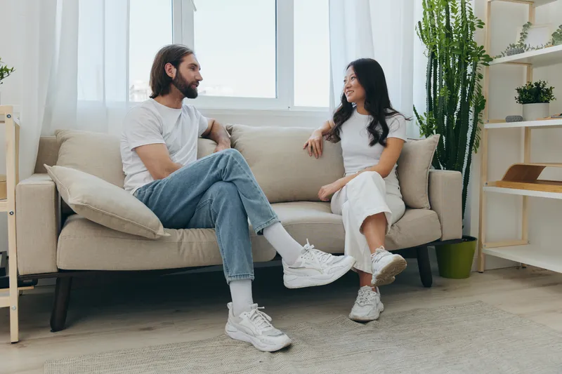 Азиатские друзья, парень и девушка, сидят на диване и весело общаются друг с другом, улыбаясь и хорошо проводя время вместе