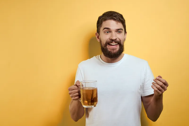 Мужчина с кружкой пива на жёлтом фоне, белая футболка, эмоции, свободное пространство