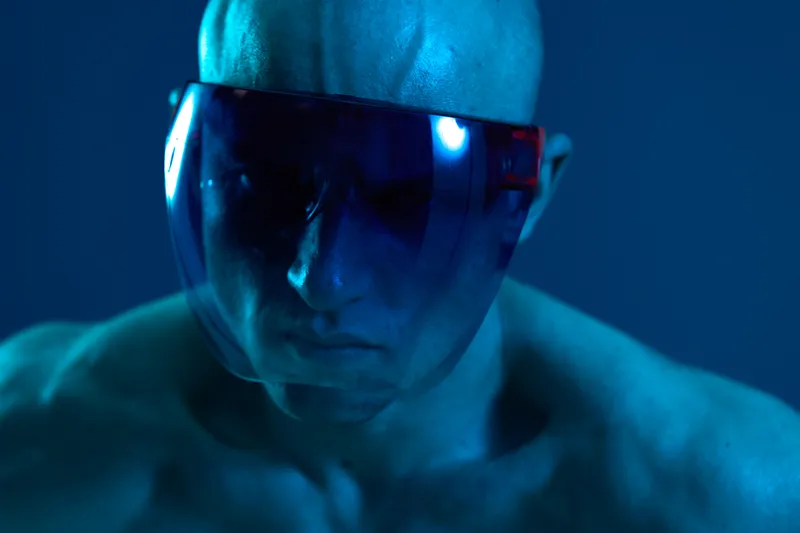 Intense man with futuristic visor, showcasing strong facial features and captivating expression against a blue background. Ideal for technology or fashion themes.