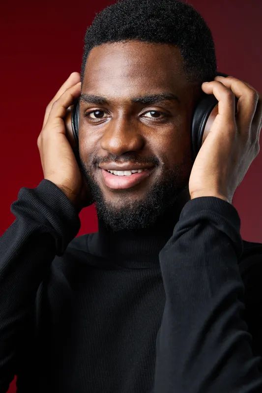 Young African man enjoying music with headphones in a cozy, vibrant setting, showcasing positive emotions and a contemporary style