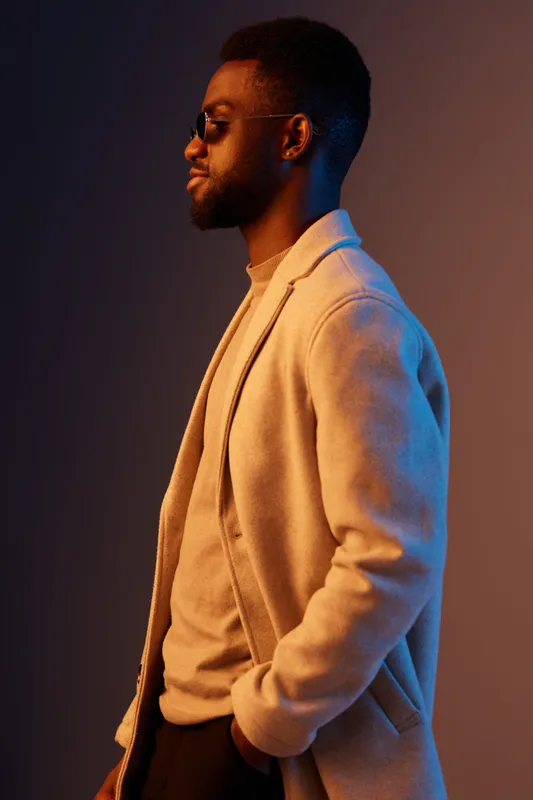 Stylish young Black man posing in a fashionable coat against a vibrant background, showcasing confidence and modern fashion trends during the autumn season