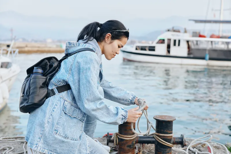 Woman dock harbor rope boat exploration travel, showing waterfront activity at a busy harbor, preparing a mooring line beside vessels, capturing travel spirit and coastal work by the sea