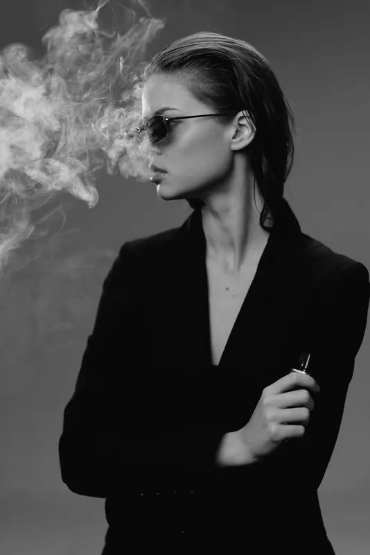 Stylish woman vaping with sunglasses in black and white portrait with smoke background