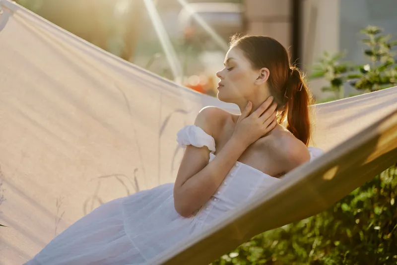 Young woman in a white dress relaxing in a hammock during golden hour, showcasing tranquility and nature s beauty Emotionally serene and peaceful