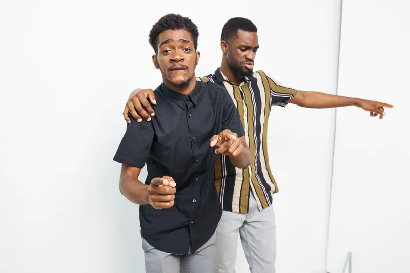 Two joyful black men dancing together in a bright studio, showcasing a lively atmosphere and authentic friendship. Their playful poses capture the essence of celebration.