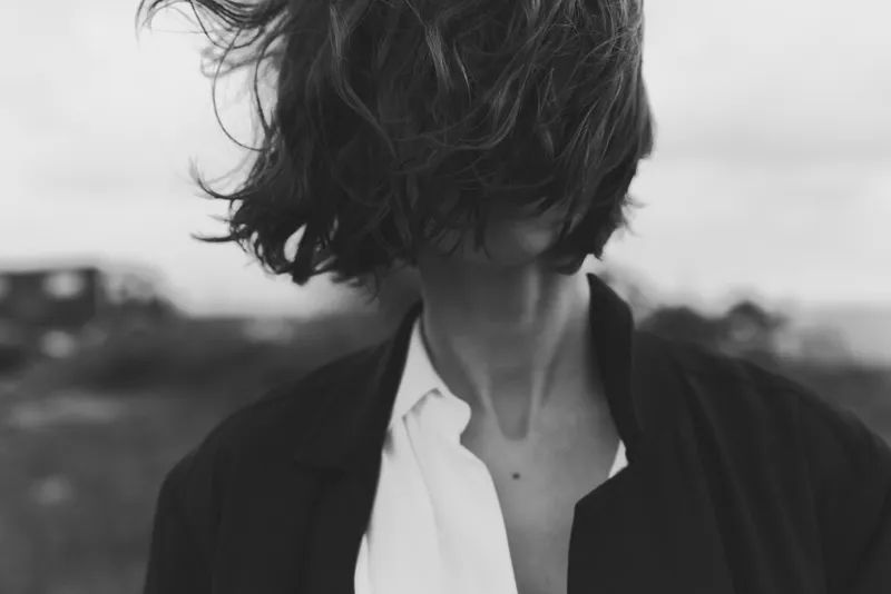 Monochrome fashion image of wind swept hair veiling the face, blazer over a white shirt, outdoor setting, moody and minimalistic, cinematic lighting, creative silhouette, artistic urban style,