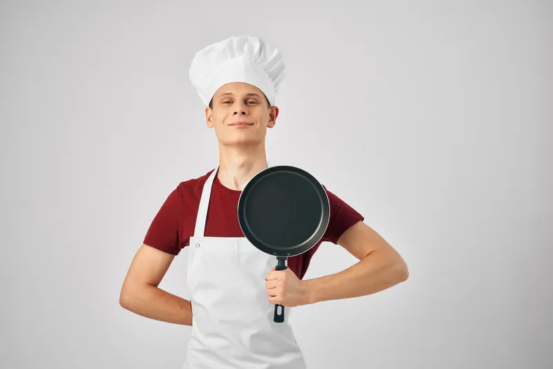Повар в униформе держит в руках сковороду на профессиональной кухне ресторана